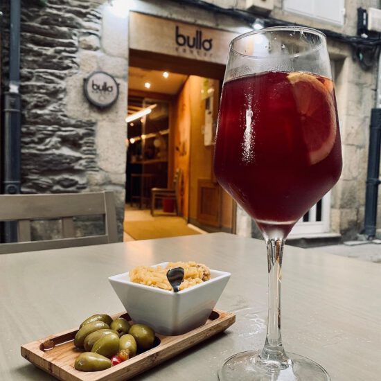 Copa de sangría con aceitunas y aperitivos en mesa de terraza de restaurante Bullo.